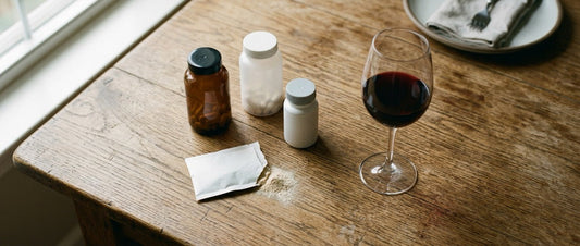 Several hangover prevention pill bottles and powder packets arranged next to a glass of wine on a wood table