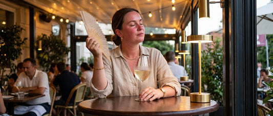 Woman in her 40s fanning her face with her hand at a dinner table with a glass of wine