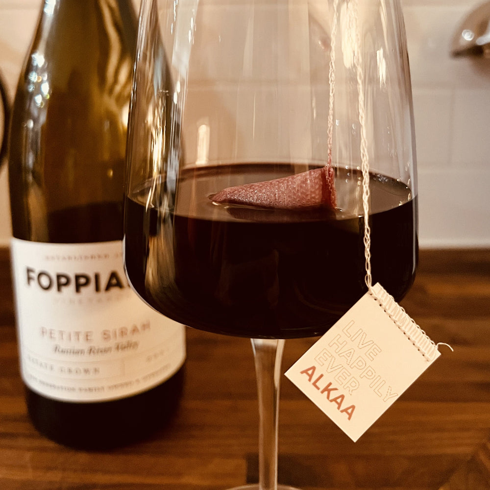 Foppiano Petite Sirah in a wine glass with an ALKAA sachet on a wood surface.